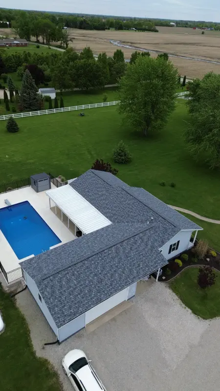 Drone view of a finished roof replacement — blue-gray architectural shingles on a country ranch home with a backyard pool